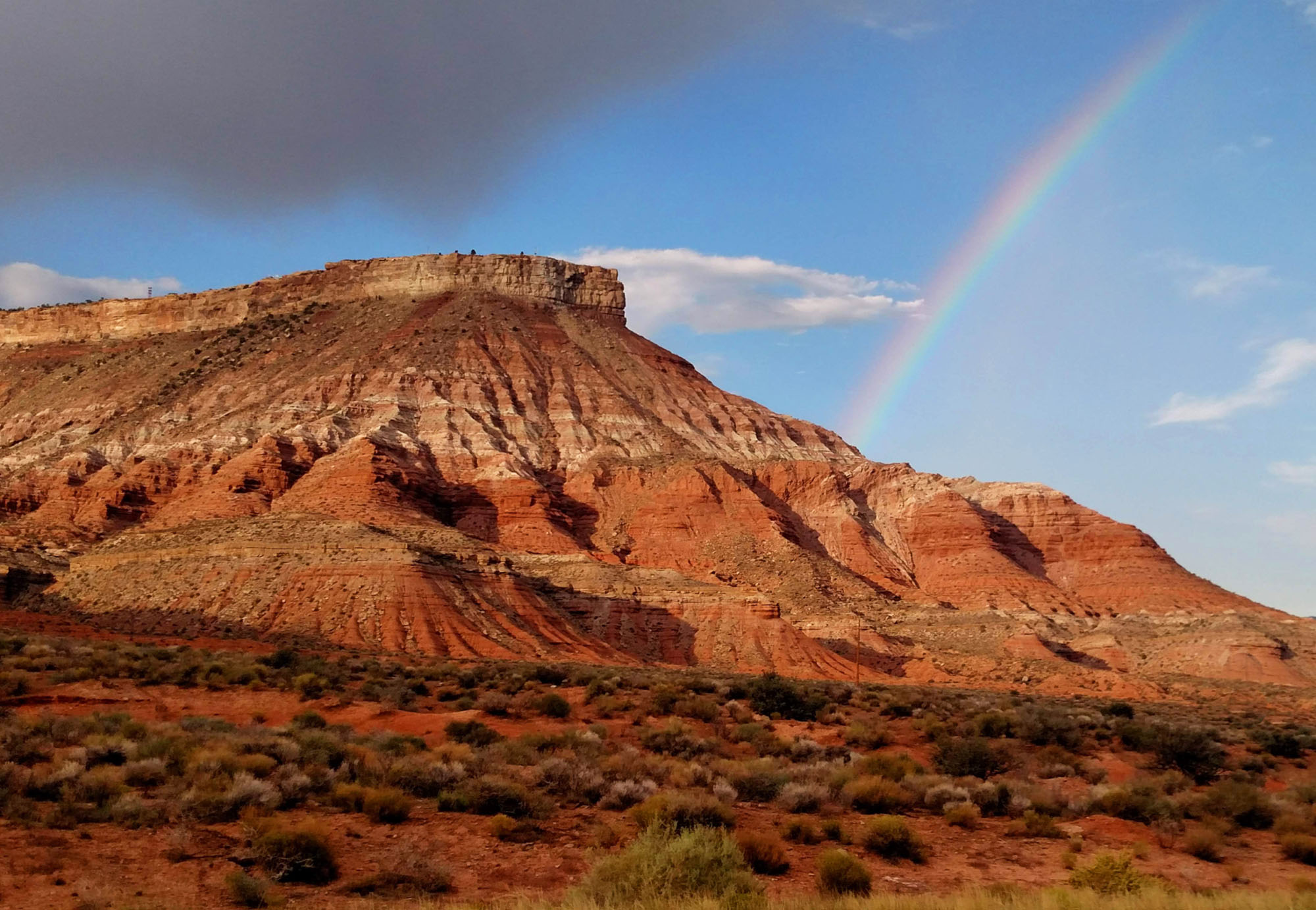 A vibrant rainbow arches over the stunning red cliffs and rugged desert landscape near Settlers Point RV Resort in Southern Utah.