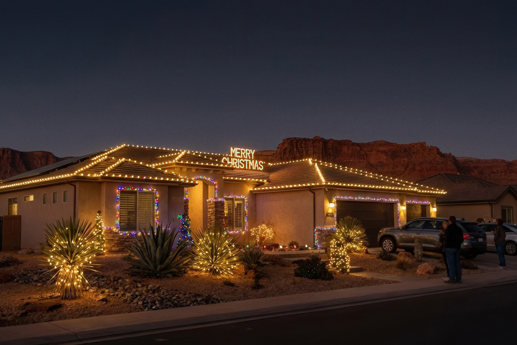 Illuminated neighborhood home featuring Christmas lights St George Utah with glowing desert plants and red rock cliffs in background.