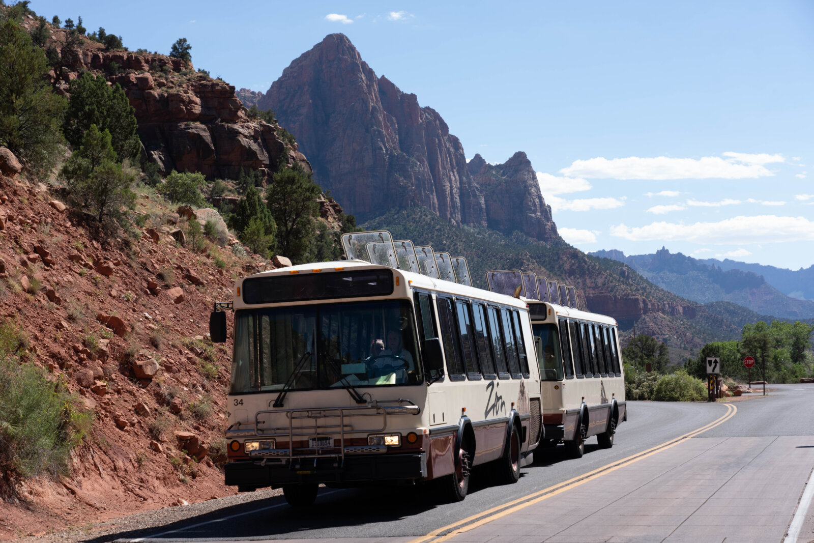 A scenic landscape of towering red rock mountains and a winding hiking trail, with a large tour bus on the road.