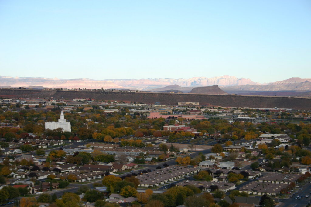 Aerial view of a sprawling residential neighborhood with a white building surrounded by autumn-colored trees and rocky ridgelines in the background.