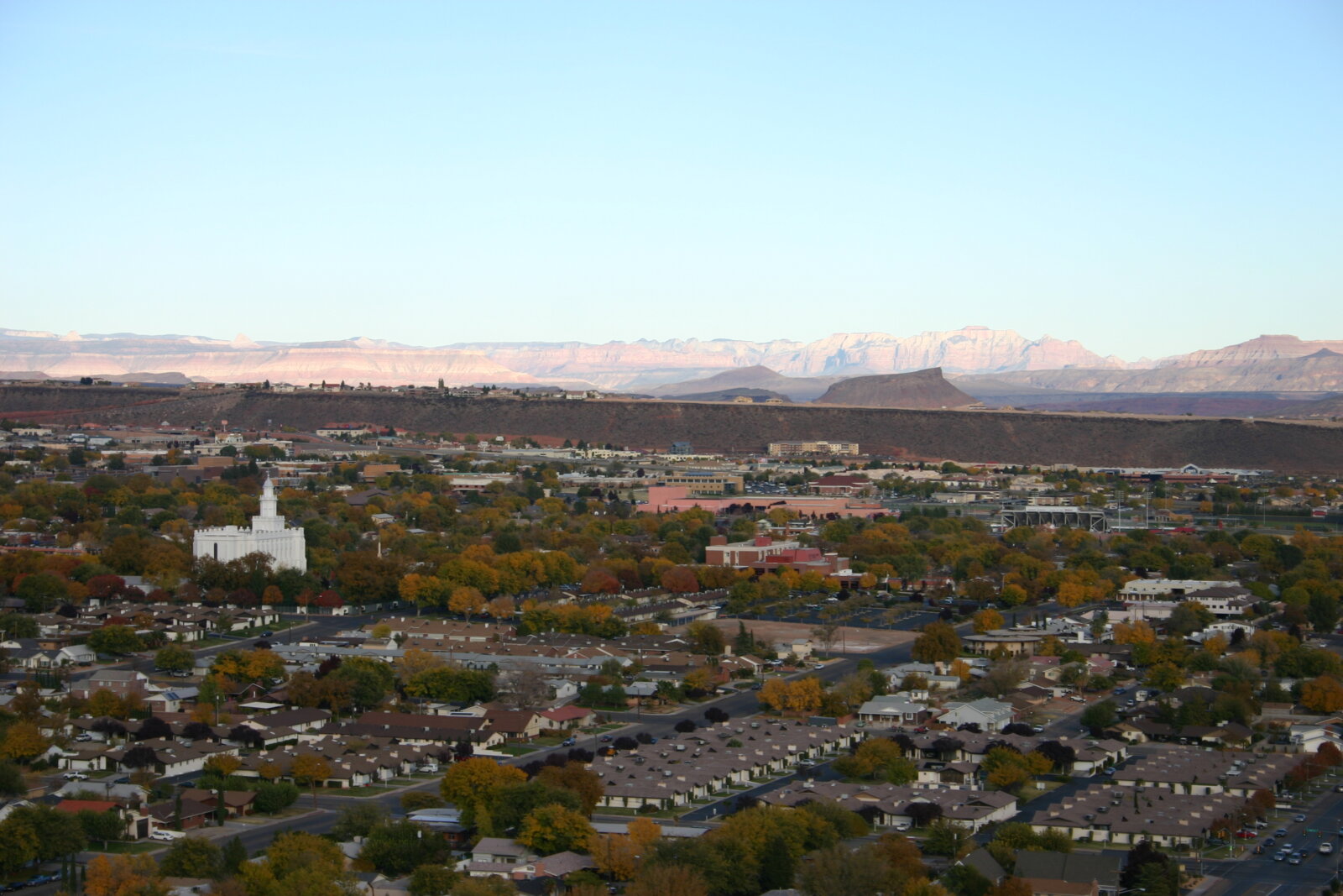 Aerial view of a sprawling residential neighborhood with a white building surrounded by autumn-colored trees and rocky ridgelines in the background.