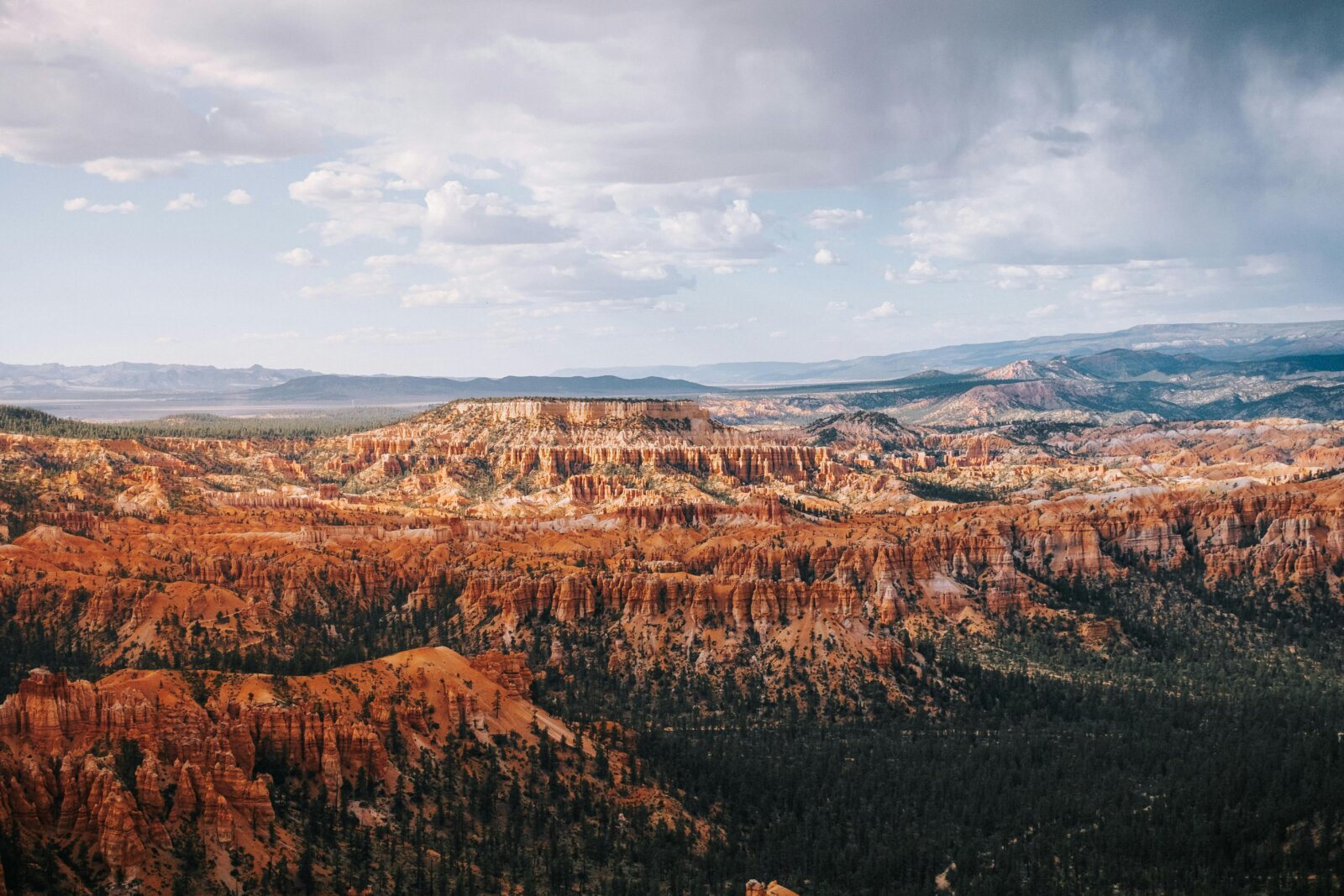 Expansive view of towering red rock spires and hoodoos stretching across a wide rugged landscape under a partly cloudy sky.