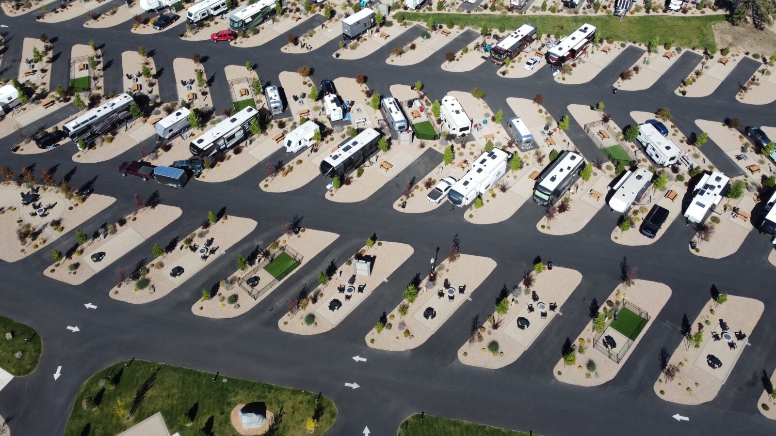 Aerial view of an RV resort with rows of paved campsites and landscaped spaces occupied by motorhomes and trailers.