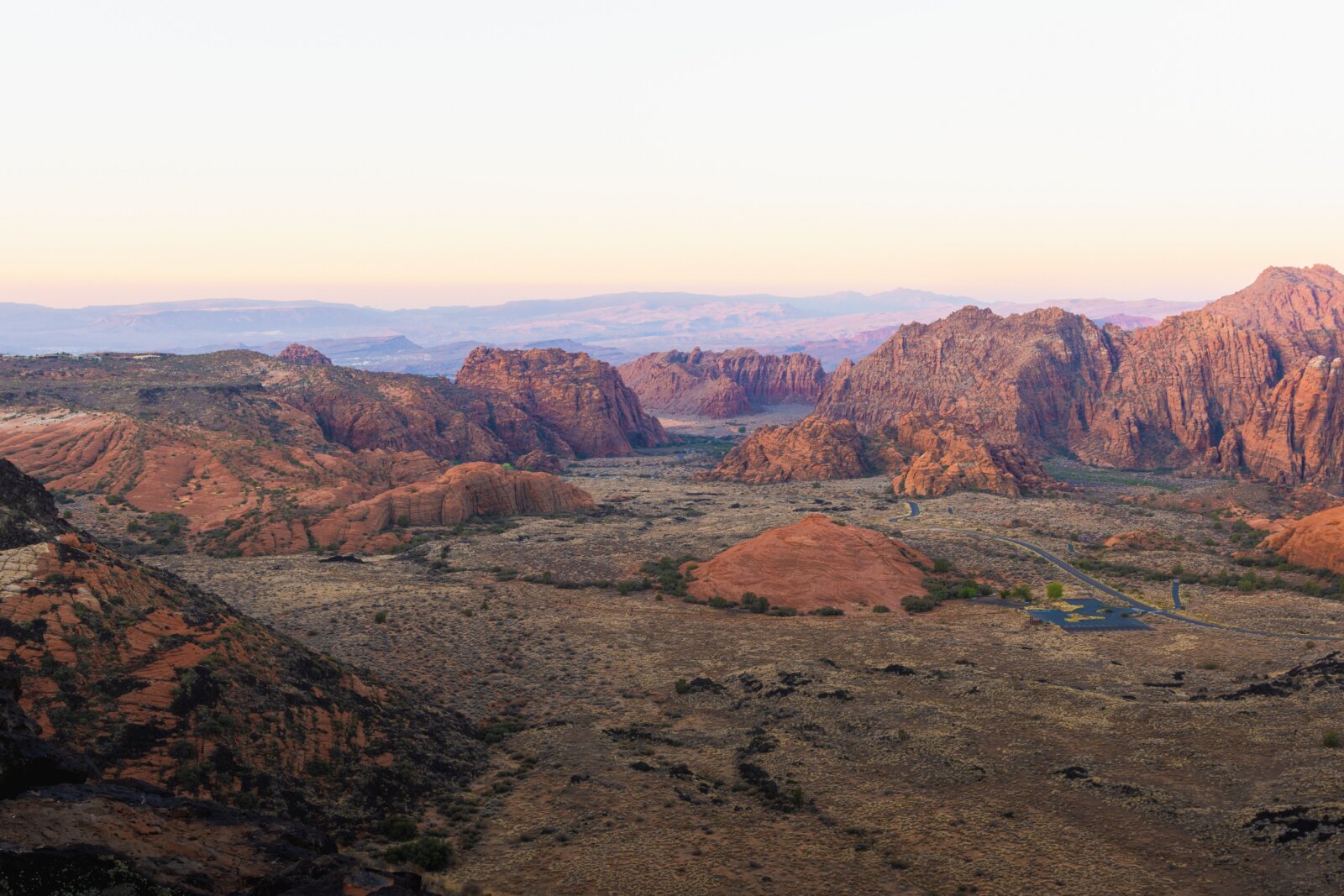 A vast rocky landscape with layered red rock formations stretching toward distant mountains at dusk.