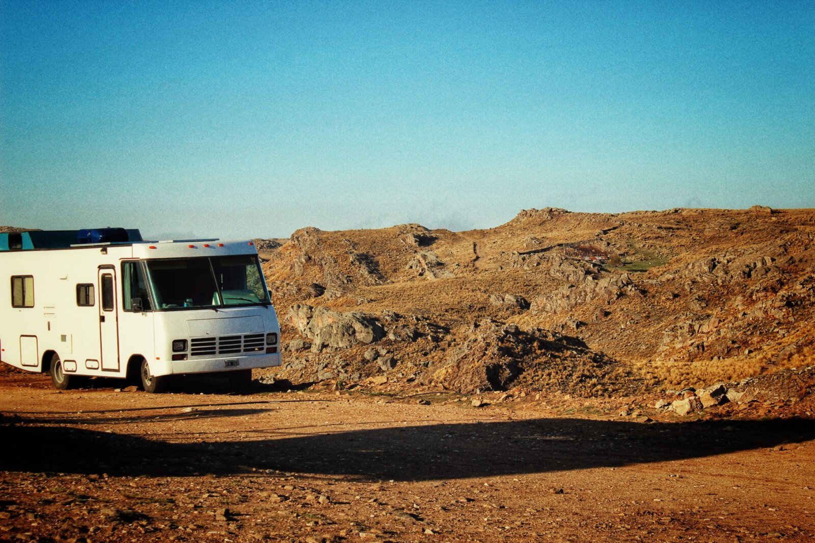 RV parked in a sunny rocky desert landscape under a clear blue sky near Southern Utah
