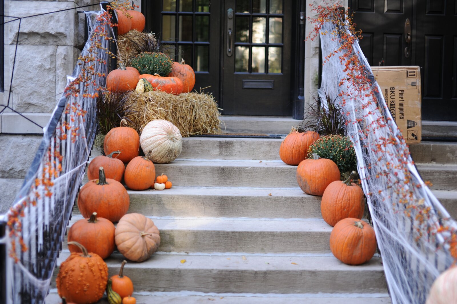 A front porch decorated with carved pumpkins, hay bales, and orange gourds for the Halloween season.